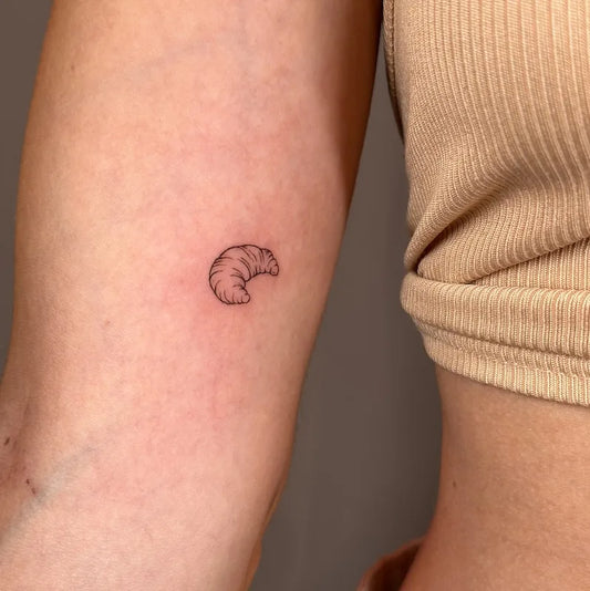 Small croissant fine line minimalist tattoo on woman bicep