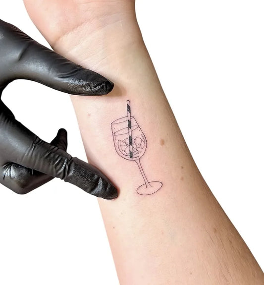 a glass of lemon drink cocktail with straw outline fine line tattoo on wrist