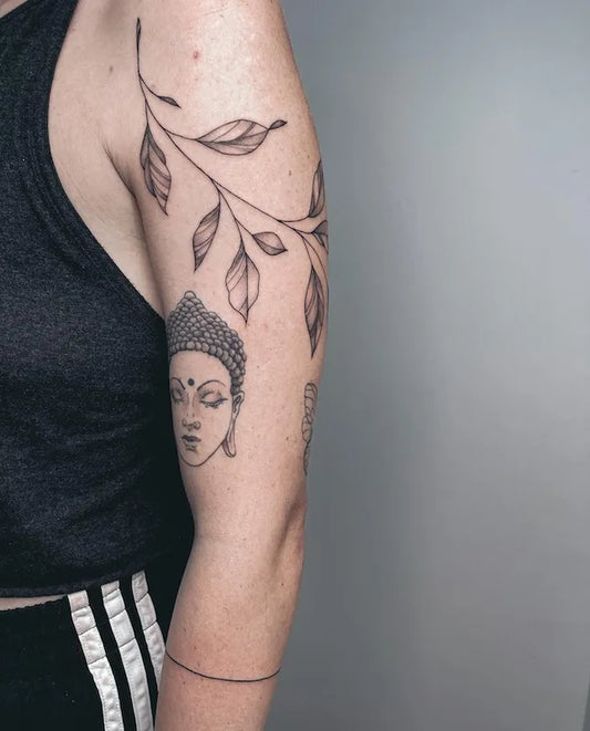 black and grey tattoo of a Buddha face and leaves on woman upper arm