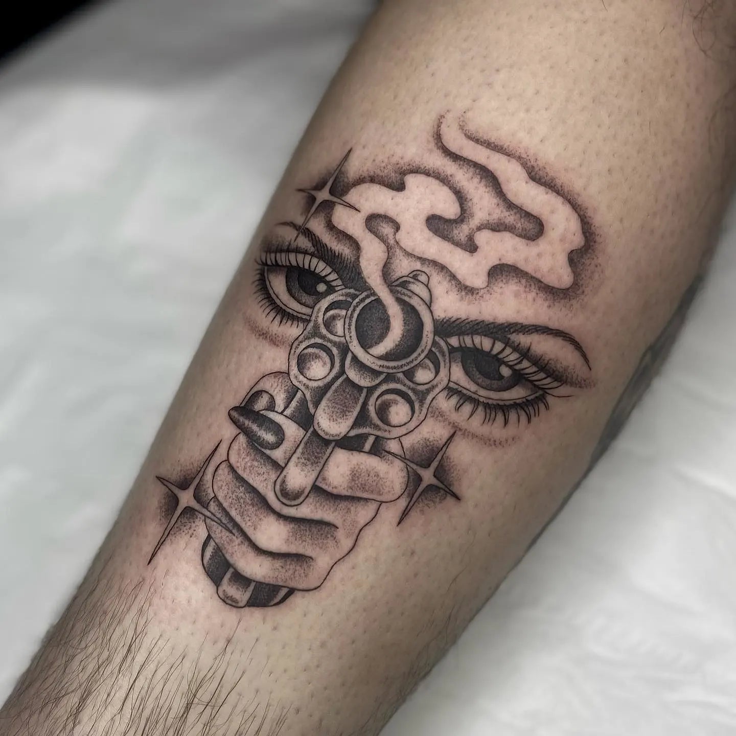 Tattoo of a hand holding a gun with eyes and smoke