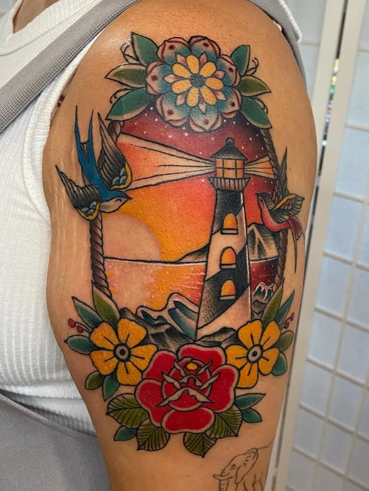 Big American Traditional Lighthouse with Sunset and Flowers Tattoo on Women Arm by @dale.tattoos