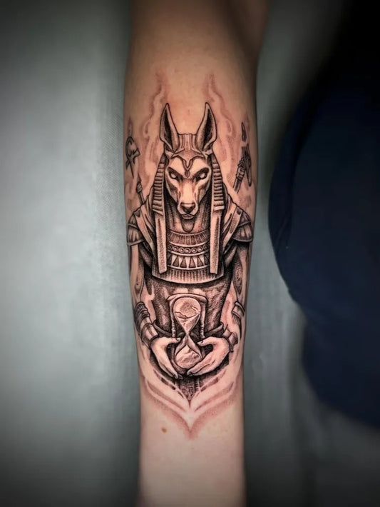 Big Black and Grey Anubis Holding Hourglass Tattoo on Women Arm by @julia_sokulska