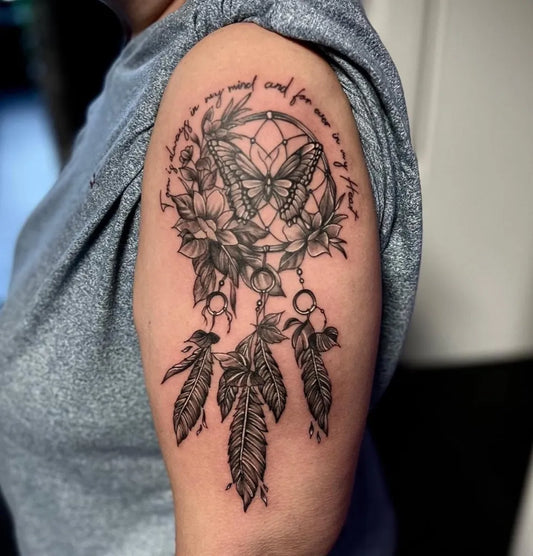 Big Black and Grey Dream Catcher with Butterfly and Flowers Tattoo on Women Upper Arm by @trauma_tattoo_essen