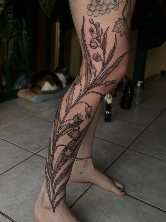 Big Black and Grey Lily of the Valley Flowers and Leaves on Women Leg Tattoo by @manders.art