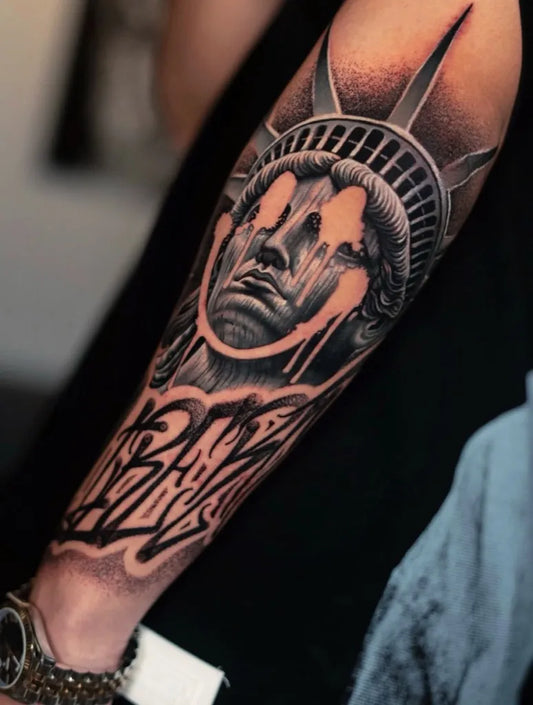 Big Black and Grey Statue of Liberty with Dripping Face and Baby Script Tattoo on Men Arm by @lamanigancetattootoronto