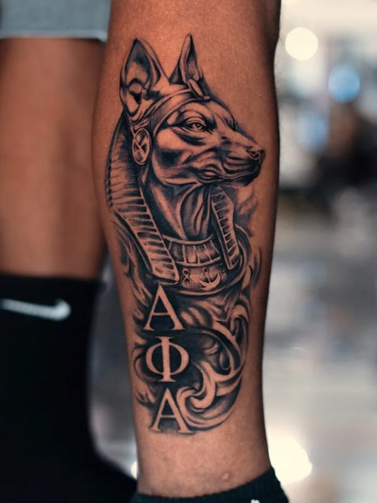 Big Blackwork Anubis Greek Letters Tattoo on Men Leg by @tattoo_dzhyhov