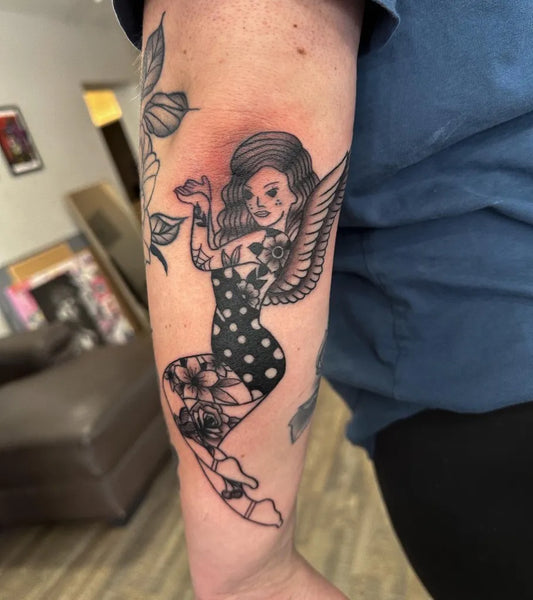 Big Blackwork Pin Up Girl with Wings and Flowers Tattoo on Women Arm by @ashli.w.tattoos