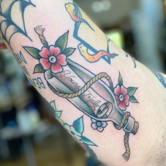 Medium American Traditional Message in a Bottle with Flowers Nautical Tattoo on Women Arm by @montgomerytattoos