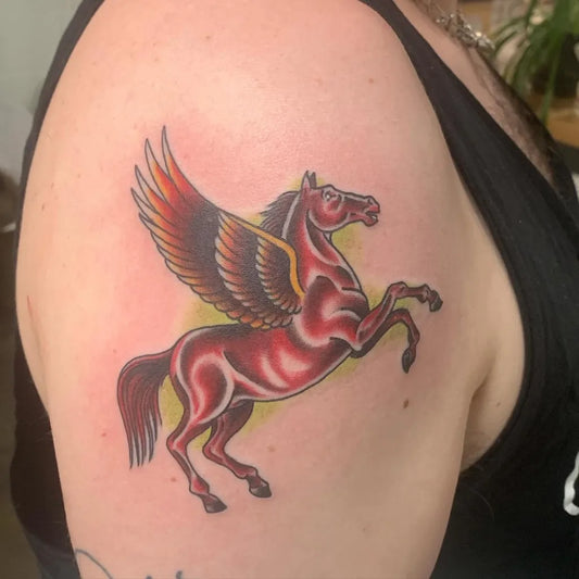 Medium American Traditional Pegasus Tattoo on Women Bicep by @sweetneedlestattoo
