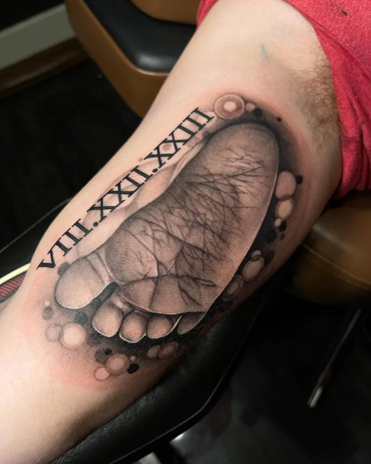 Medium Black and Grey Baby Footprint Tattoo on Men Bicep by @undertheneedleaz
