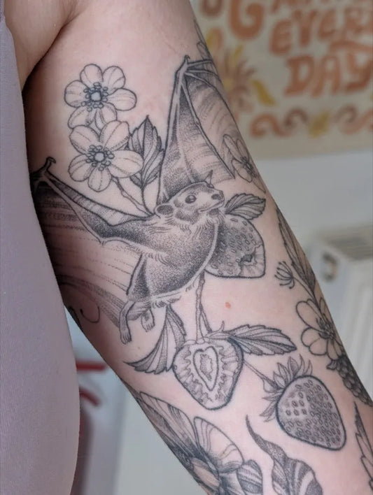 Medium Black and Grey Bat Strawberry Flowers Tattoo on Women Arm by @gina.v.tattoos
