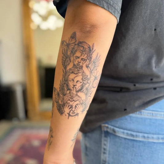 Medium Black and Grey Cherub and Flowers Tattoo on Women Arm by @emma.pokeya