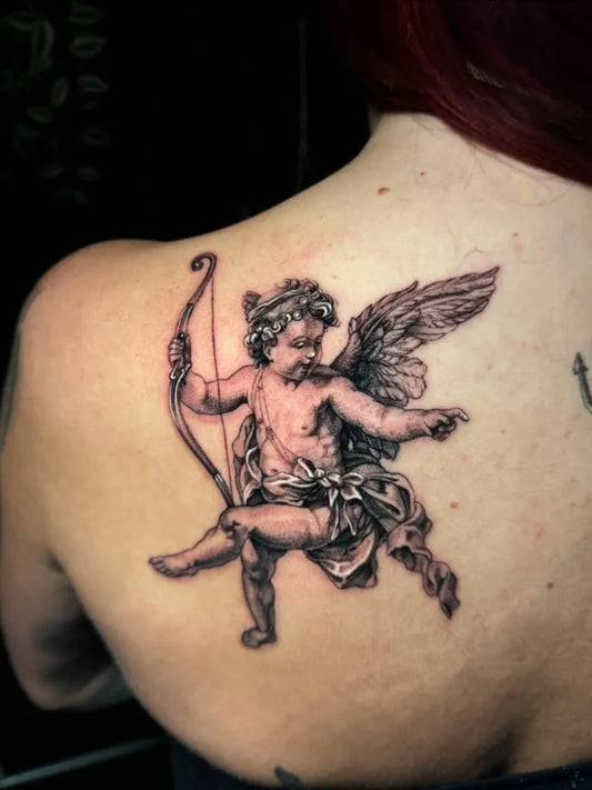 Medium Black and Grey Cherub with Bow and Wings Tattoo on Women Shoulder by @thebrzy.tattoo