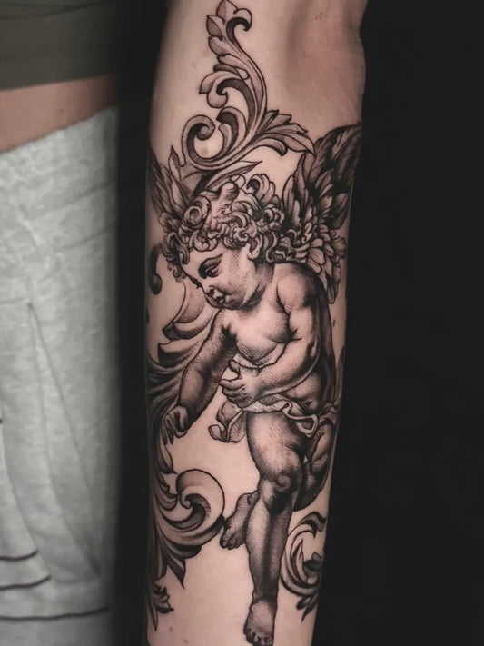 Medium Black and Grey Cherub with Ornamental Wings Tattoo on Women Arm by @oldlondonroadtattoos