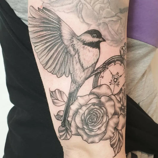 Medium Black and Grey Chickadee Clock Rose Tattoo on Women Arm by @lucia_mayer_tattoo