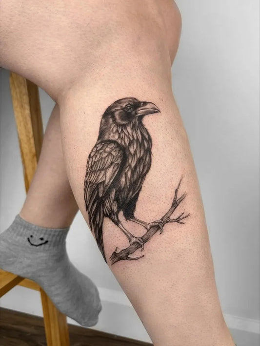Medium Black and Grey Crow on Branch Tattoo on Women Leg by @nikie.tatoueuse