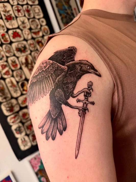 Medium Black and Grey Crow with Skull and Sword Tattoo on Men Shoulder by @alystattoos