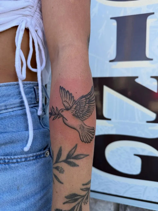 Medium Black and Grey Dove with Olive Branch Tattoo on Women Arm by @inktherapywithkatie