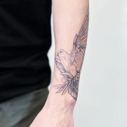 Medium Black and Grey Dove with Wings and Leaves Tattoo on Men Arm by @emerald_artistrystudio