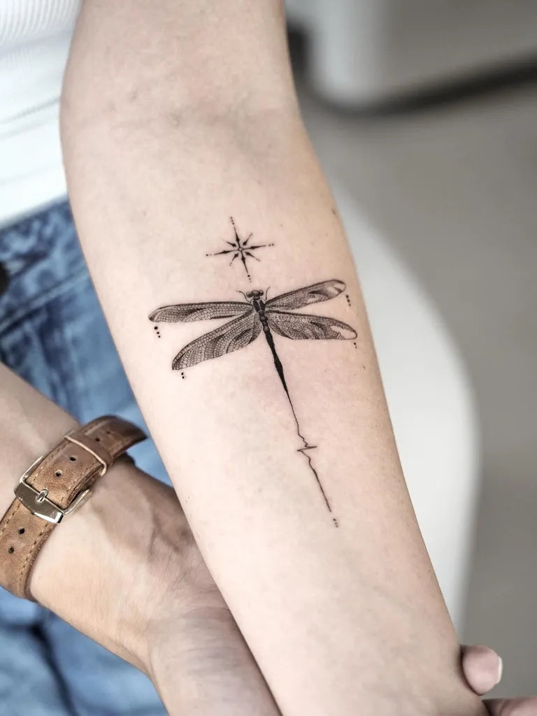 Medium Black and Grey Dragonfly with North Star on Women Arm Tattoo by @dominikzky.tattoo