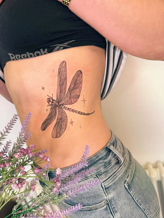 Medium Black and Grey Dragonfly with Stars and Lavender on Women Rib Tattoo by @ladyrosetattoos