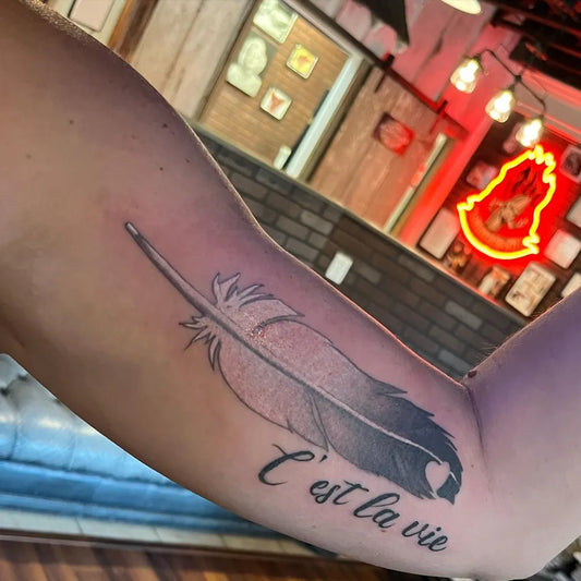 Medium Black and Grey Feather with Quote Tattoo on Women Bicep by @bullett_ink