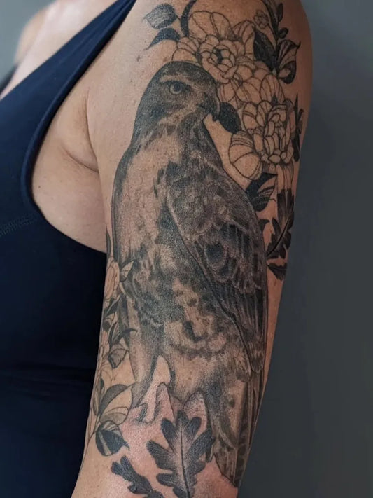 Medium Black and Grey Hawk and Flowers Tattoo on Women Upper Arm by @faelien.ink