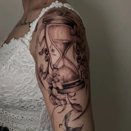 Medium Black and Grey Hourglass and Flowers Tattoo on Women Shoulder by @maria_i_tattooartist