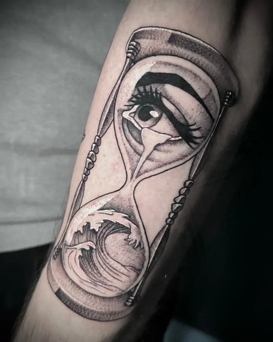 Medium Black and Grey Hourglass with Eye and Waves Tattoo on Men Arm by @breakdown.tattoo