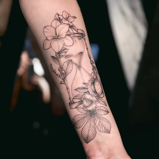 Medium Black and Grey Hourglass with Flowers and Leaves Tattoo on Women Arm by @invictaink