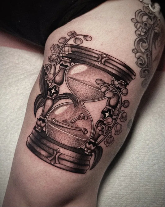 Medium Black and Grey Hourglass with Lilies Tattoo on Women Thigh by @dollheart.tattoos