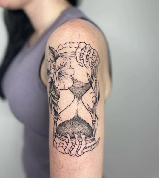 Medium Black and Grey Hourglass with Skeleton Hands and Flowers Tattoo on Women Upper Arm by @abryvtattoos