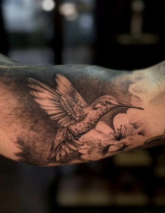 Medium Black and Grey Hummingbird and Flowers Tattoo on Women Arm by @roomcraft.tattoo