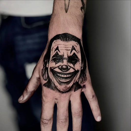 Medium Black and Grey Joker Face on Men Hand Tattoo by @emilianoronatattoo