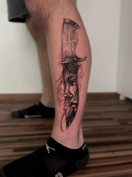 Medium Black and Grey Knife with Face Tattoo on Men Leg by @travel_and_tattoo
