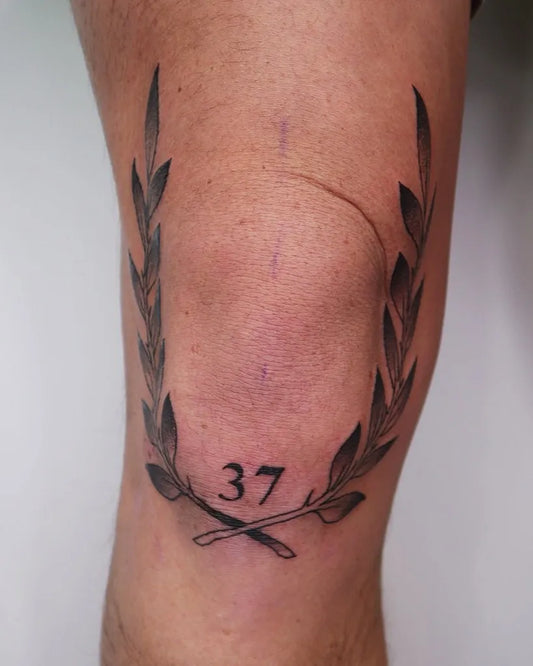 Medium Black and Grey Laurel Wreath with Number Tattoo on Men Knee by @rune.ink