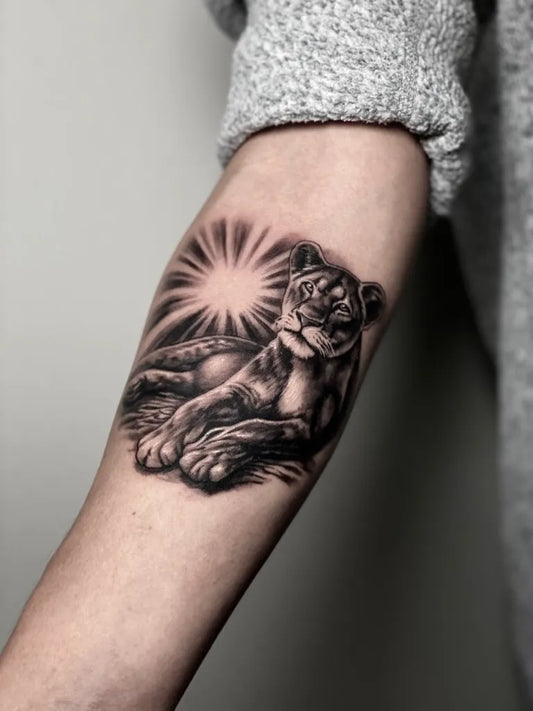 Medium Black and Grey Lion with Sunburst on Women Arm Tattoo by @lukas.desmotes.tattoo