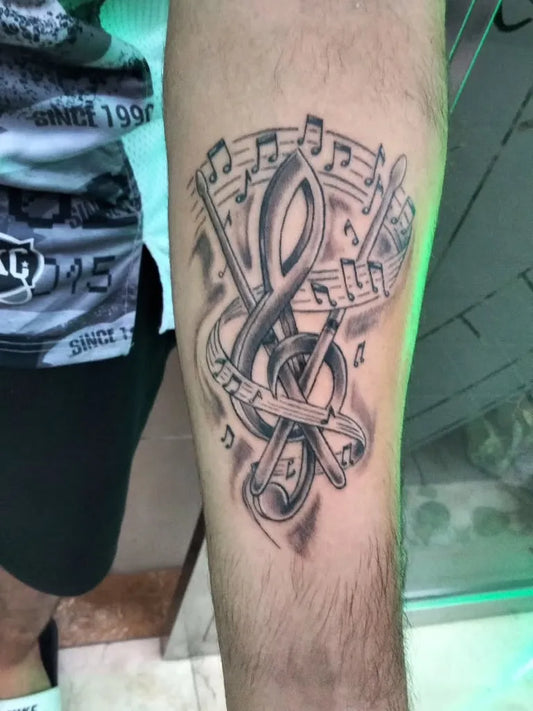 Medium Black and Grey Musical Notes Treble Clef Drumsticks Music Tattoo on Men Arm by @tooptattooalicante