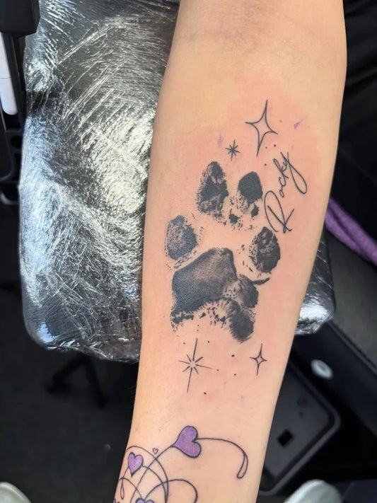 Medium Black and Grey Paw Print with Stars and Name Tattoo on Women Arm by @embracetattoo