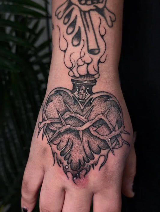 Medium Black and Grey Sacred Heart with Flames and Crown of Thorns Tattoo on Men Hand by @art_of_the_paiges