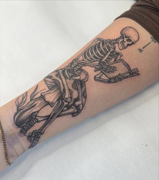 Medium Black and Grey Skeleton Reading Book Tattoo on Women Arm by @ajollytattoo