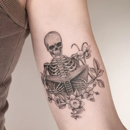 Medium Black and Grey Skeleton Reading Book with Daffodils Tattoo on Women Arm by @captainshade.tt