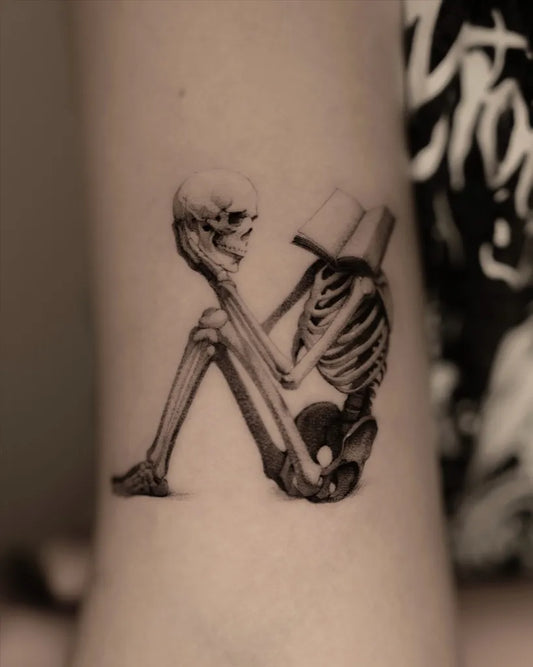 Medium Black and Grey Skeleton Reading Tattoo on Women Arm by @paradyme.ttt