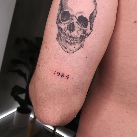 Medium Black and Grey Skull Number Tattoo on Men Arm by @alexherndzstudio