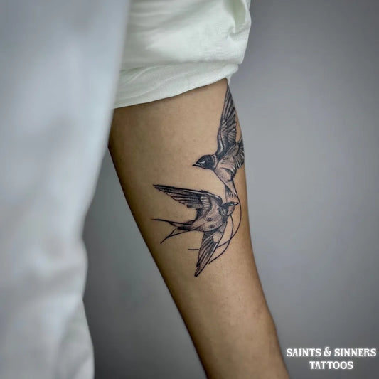 Medium Black and Grey Swallow Pair Tattoo on Women Arm by @saintsandsinnerstattooss