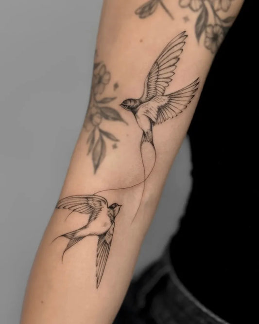 Medium Black and Grey Swallow and Flowers Tattoo on Women Arm by @a.ink.tattoo_ellie