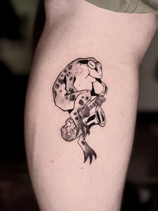 Medium Blackwork Frog Playing Saxophone Tattoo on Women Thigh by @tsukioreo.tattoo