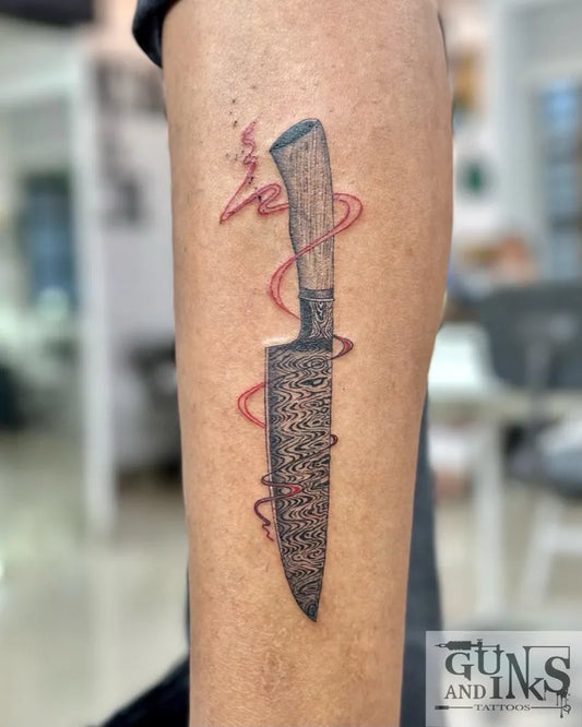 Medium Blackwork Knife with Red Ribbon Tattoo on Men Leg by @gunsandinkstattoos