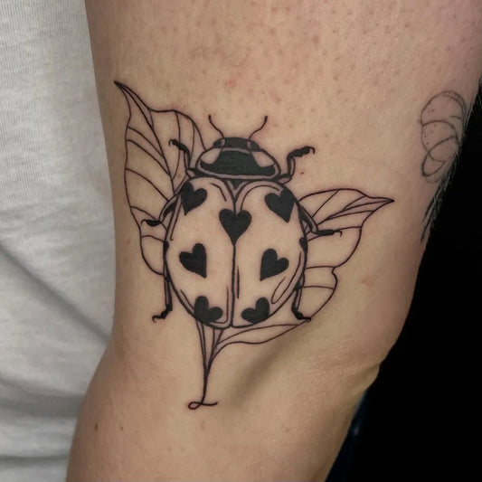 Medium Blackwork Ladybug Hearts Leaves Tattoo on Women Arm by @liquorice_ink