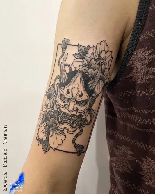 Medium Blackwork Oni Mask with Flowers on Women Arm Tattoo by @blue_heaven_tattooz